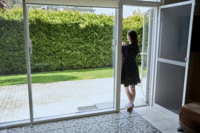 Frau öffnet Insektenschutz-Schiebetür zum Garten