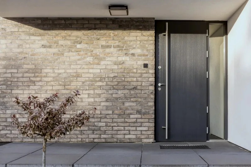 Moderne anthrazitfarbene Haustür mit Edelstahlgriff an Klinkerfassade